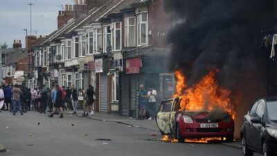 Sebuah mobil terbakar selama protes antiimigrasi di Middlesbrough, Inggris, Minggu 4 Agustus 2024. (AP/Owen Humphreys)