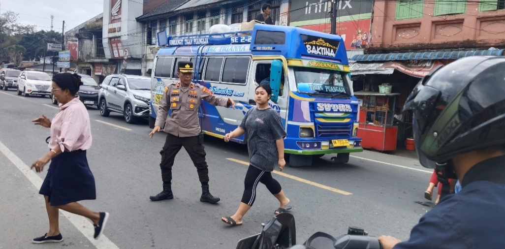 Personel polisi bantu pejalan kaki menyeberangi jalan.(ist)